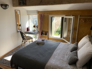 A bedroom with a bed, a desk with a chair, a window with curtains, and a mirror on the wall.
