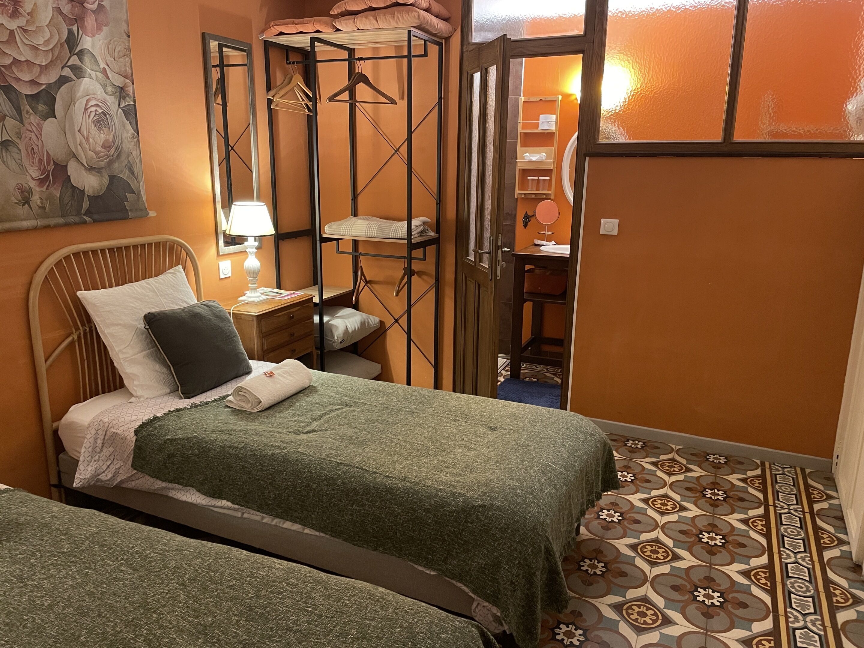 Ein Zimmer mit zwei Betten, einem Nachttisch mit Lampe, einem Kleiderschrank und einem durch eine offene Tür einsehbaren Badezimmer.