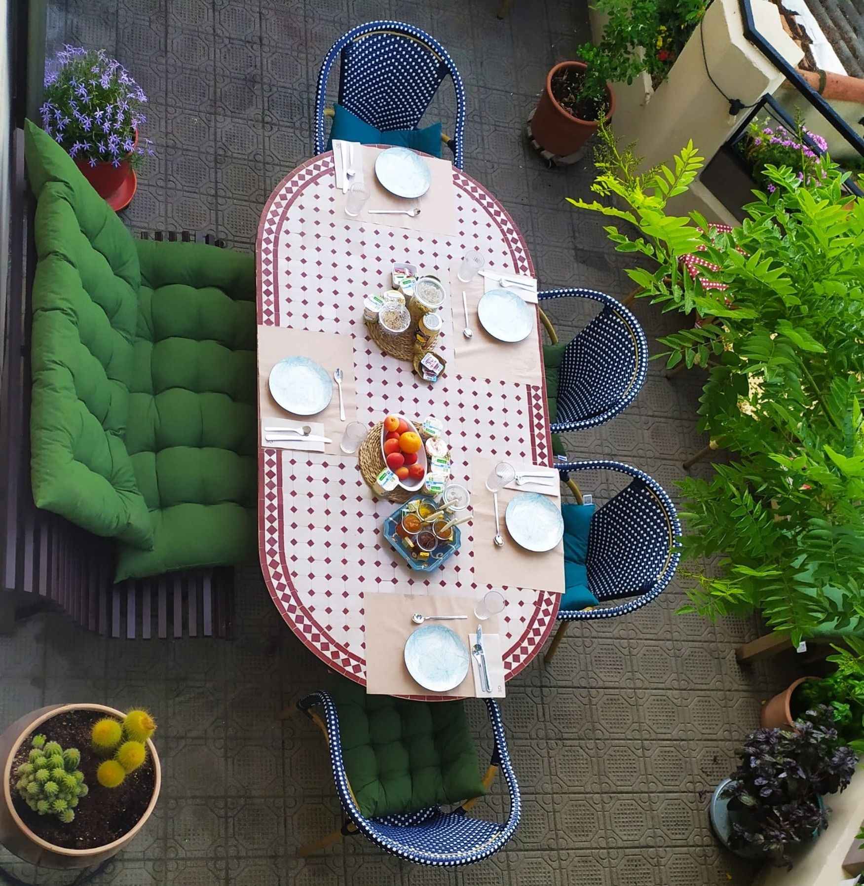 Un área de comedor al aire libre con una mesa redonda dispuesta para cuatro personas, rodeada de sillas acolchadas verdes.