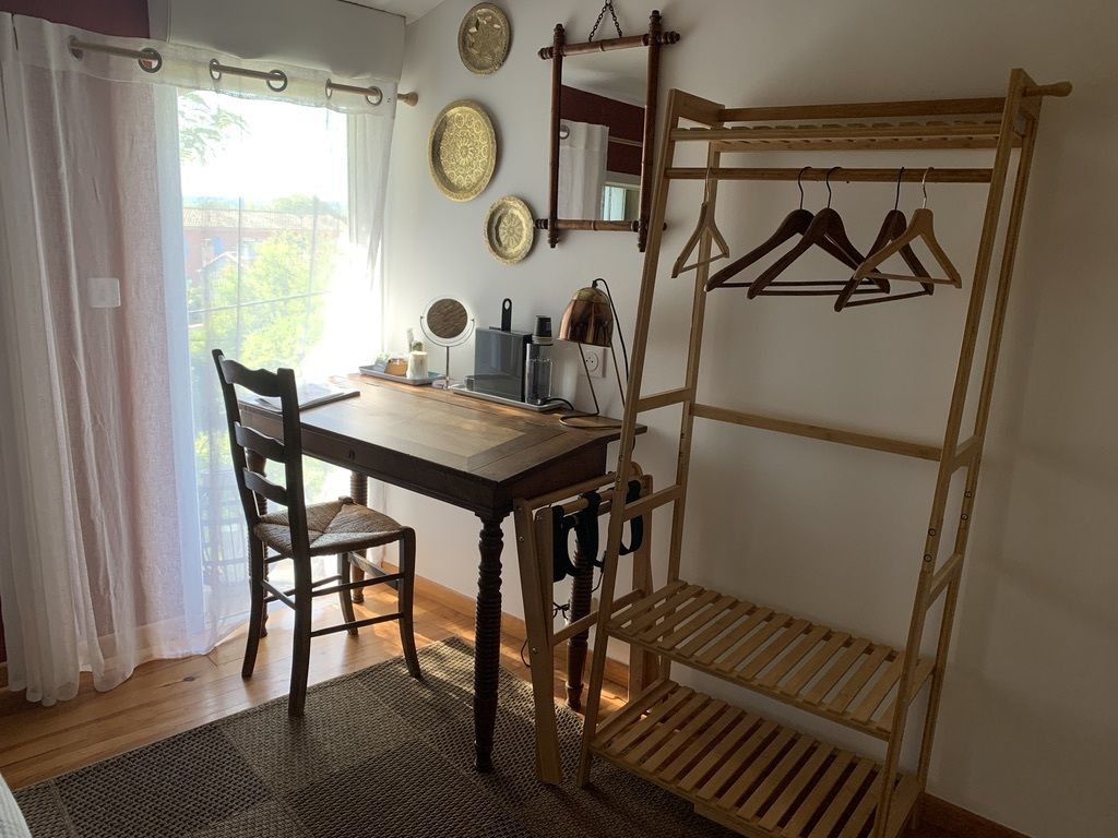 Une pièce avec une table en bois, des chaises, un portant à vêtements et des assiettes décoratives accrochées au mur.