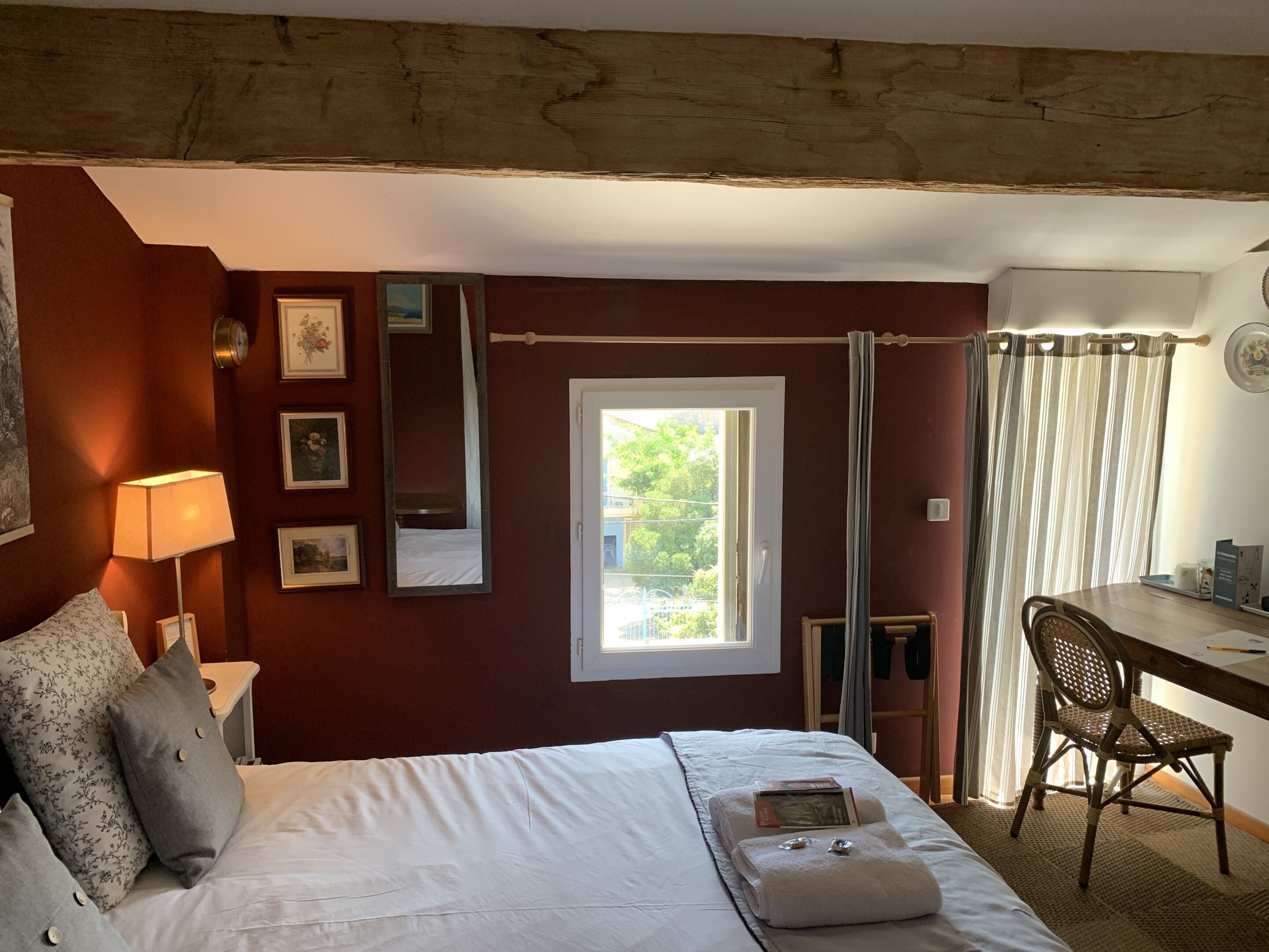 A hotel room with a bed, a desk, a chair, a window, and a door.