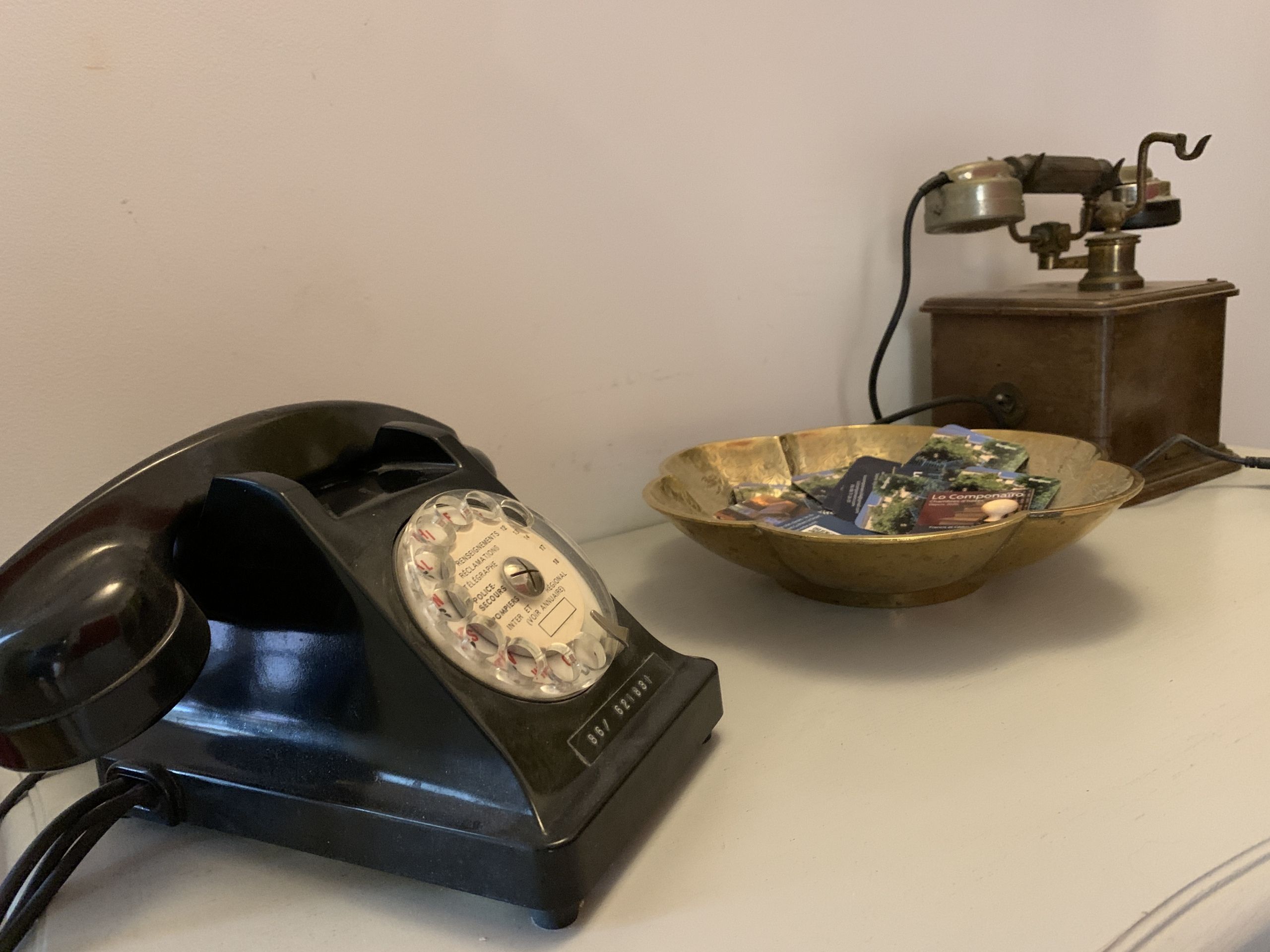 A vintage rotary dial telephone and a brass bowl with various items on a table.