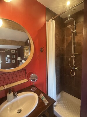 A bathroom with a white sink, a round mirror, a shower with a handheld showerhead, and a red accent wall.
