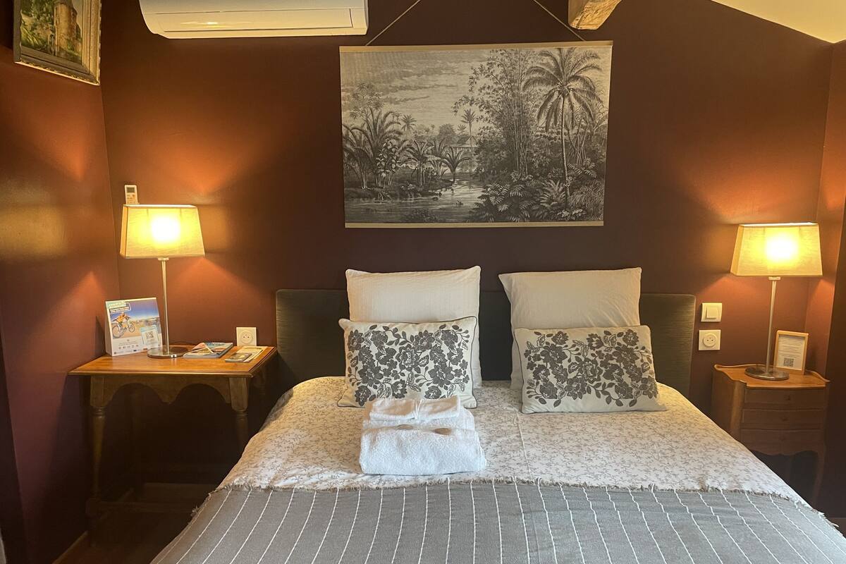 A hotel room with a bed, two nightstands, a wall-mounted air conditioner, a framed picture, and two lamps.