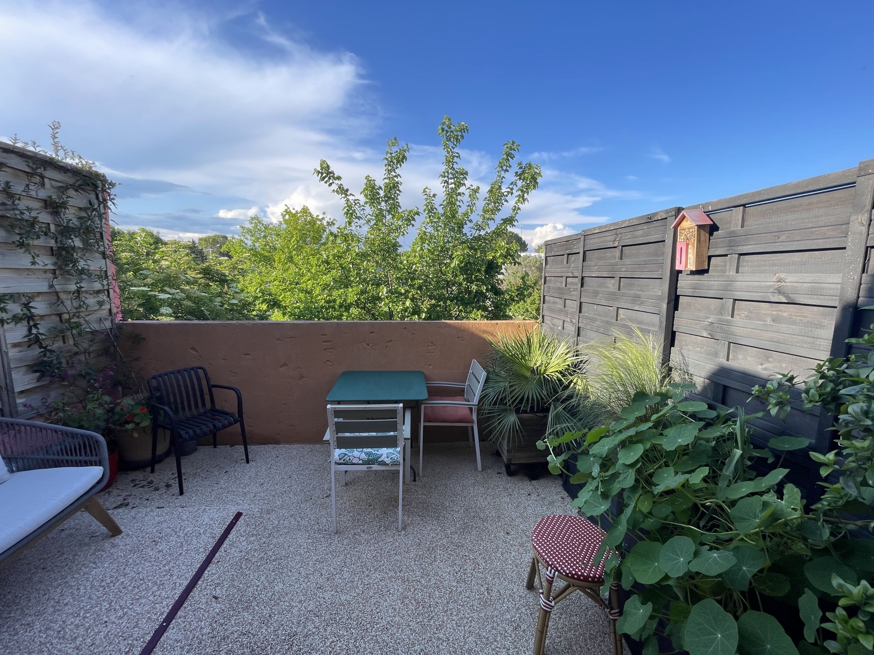 A patio area with a table and chairs, surrounded by plants and a wooden fence.