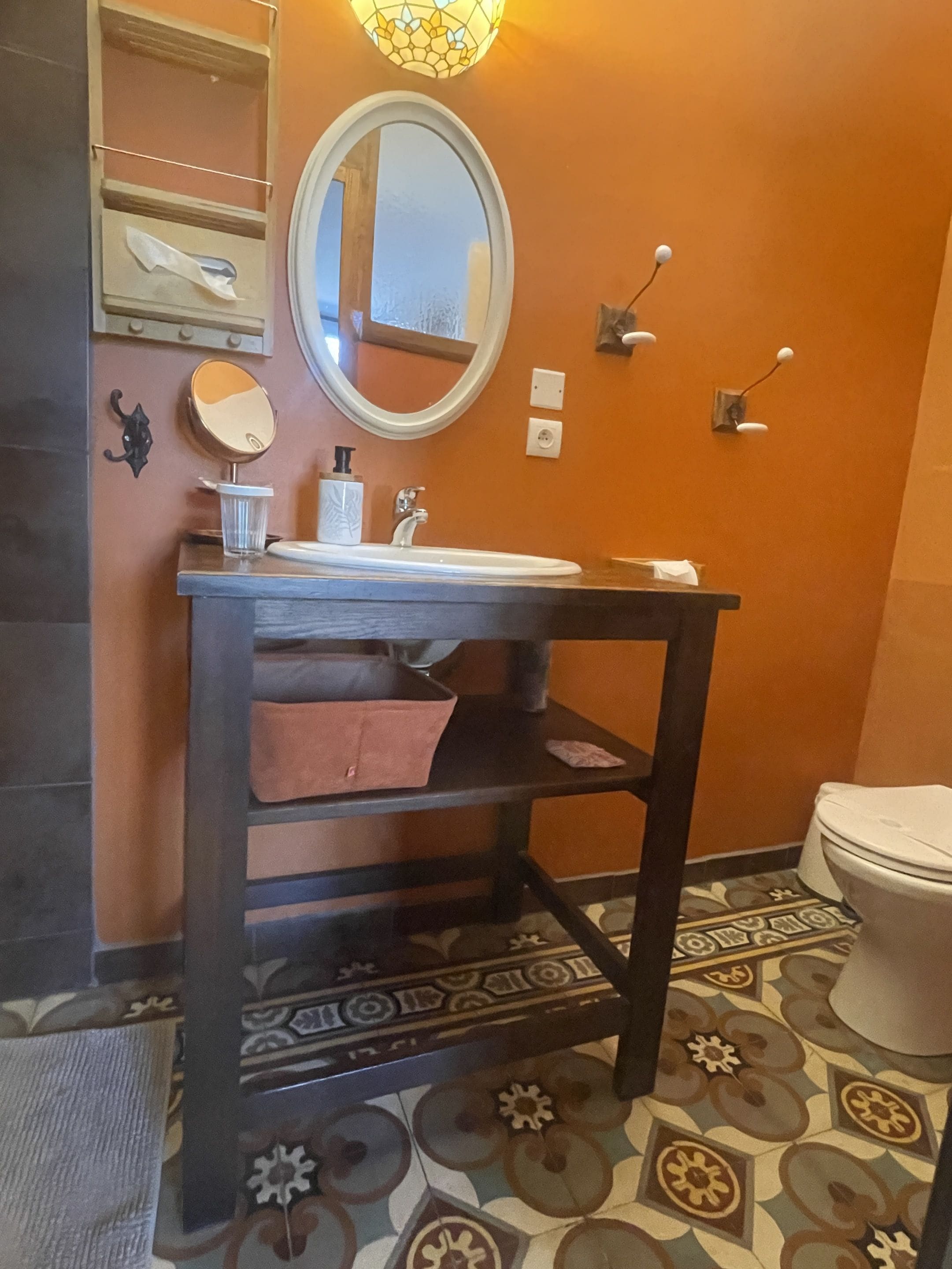 A bathroom with a round mirror, a white sink, a dark wooden vanity, and a toilet.