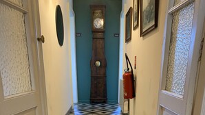 A hallway with a checkered floor, a wooden clock, and a fire extinguisher on the wall. - Lo Componaïro (Pouzols)