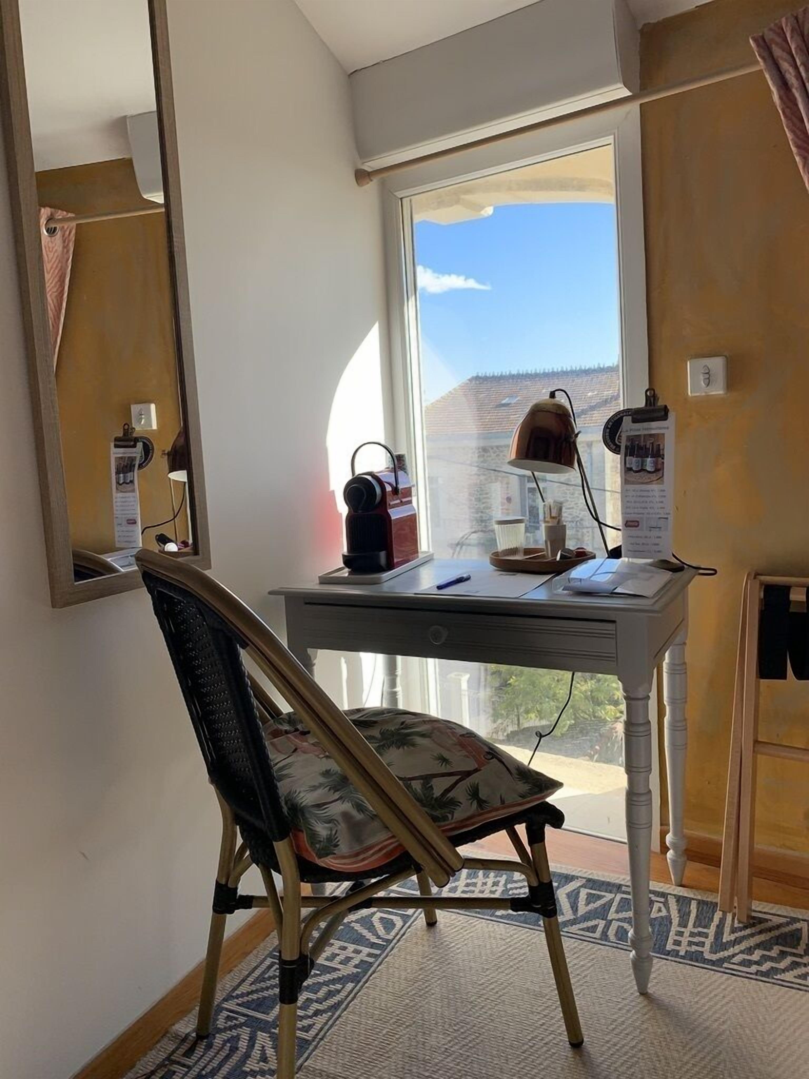 Una habitación con escritorio, silla y un ventanal con vistas a un edificio y árboles.