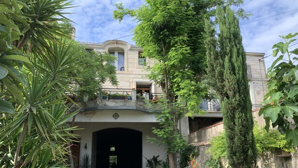 A building with a covered entrance, surrounded by lush greenery and a gravel path leading to the door. - Lo Componaïro (Pouzols)