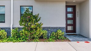 A modern building with a dark front door, a small tree, and a stone wall.