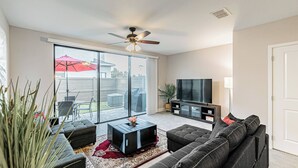 A modern living room with a sectional sofa, a flat-screen TV, and a ceiling fan.
