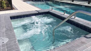 A swimming pool with a hot tub area, tiled deck, and a metal safety railing.