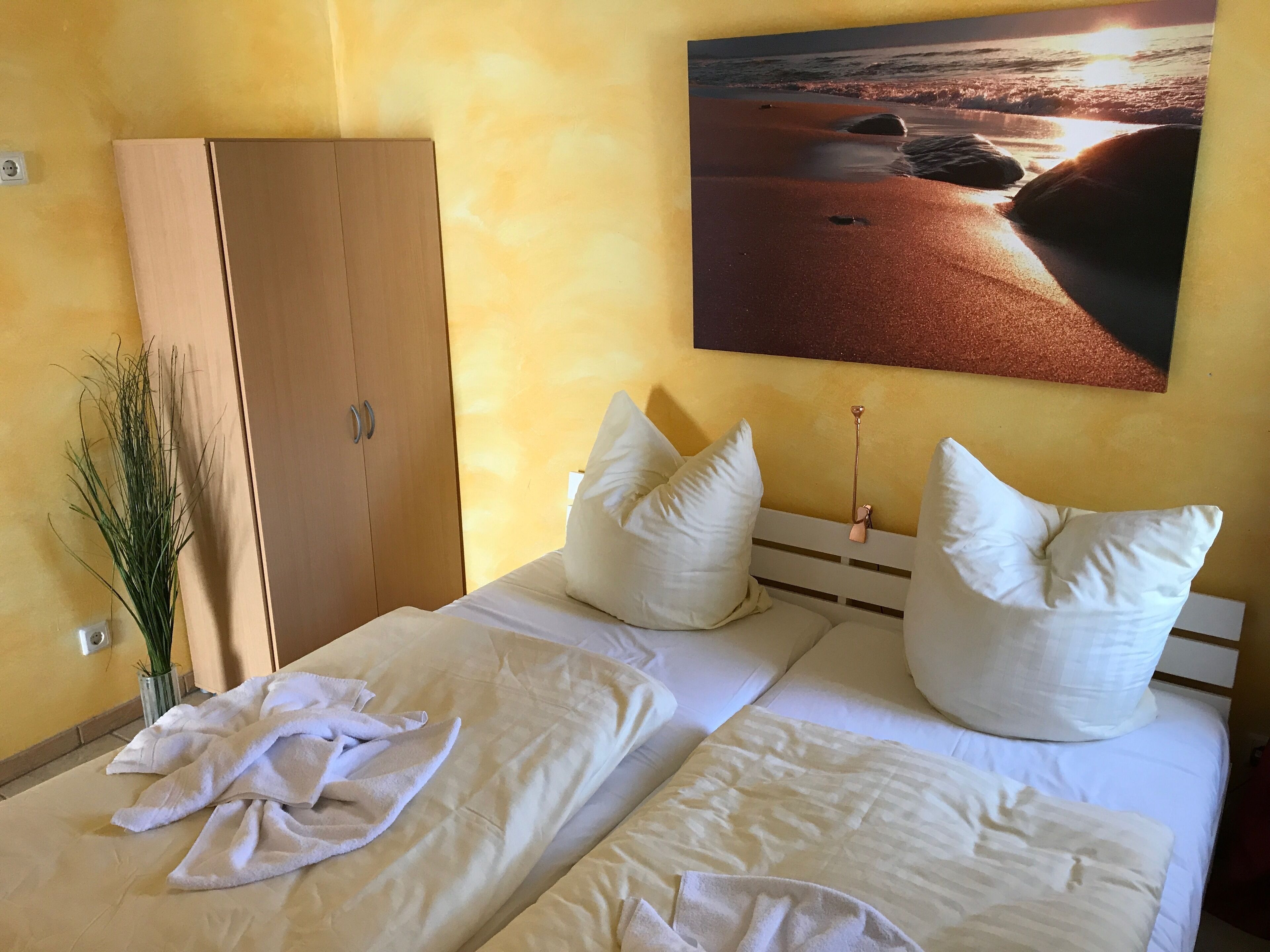 A bedroom with two beds, a wooden wardrobe, and a wall-mounted painting of a beach scene.