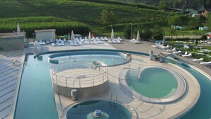 Una amplia piscina al aire libre con varias secciones y sillas de descanso.
