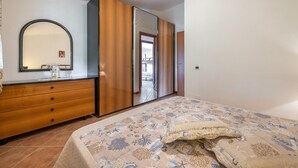 Une chambre à coucher comprenant un lit, une commode, un miroir, une armoire et donnant sur une autre pièce.