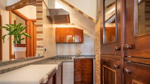 A kitchen with granite countertops, wooden cabinets, a stove, and a potted plant. - Apartment "Casa Mallus" With Mountain View, Balcony, Garden, Terrace & Grill (castiadas olia speciosa)