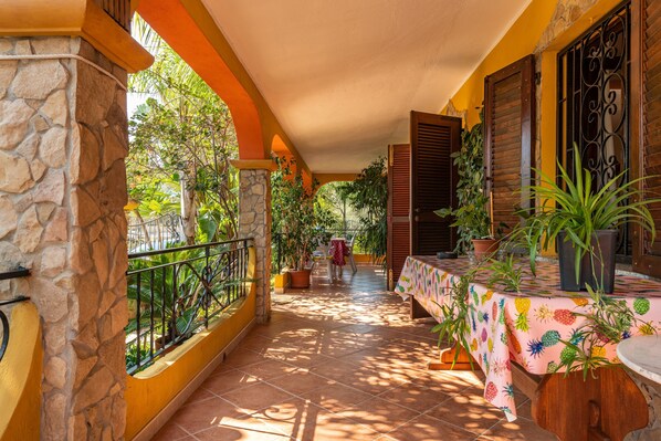 A covered outdoor area with a stone wall, a tiled floor, and a table with a pineapple-patterned tablecloth.