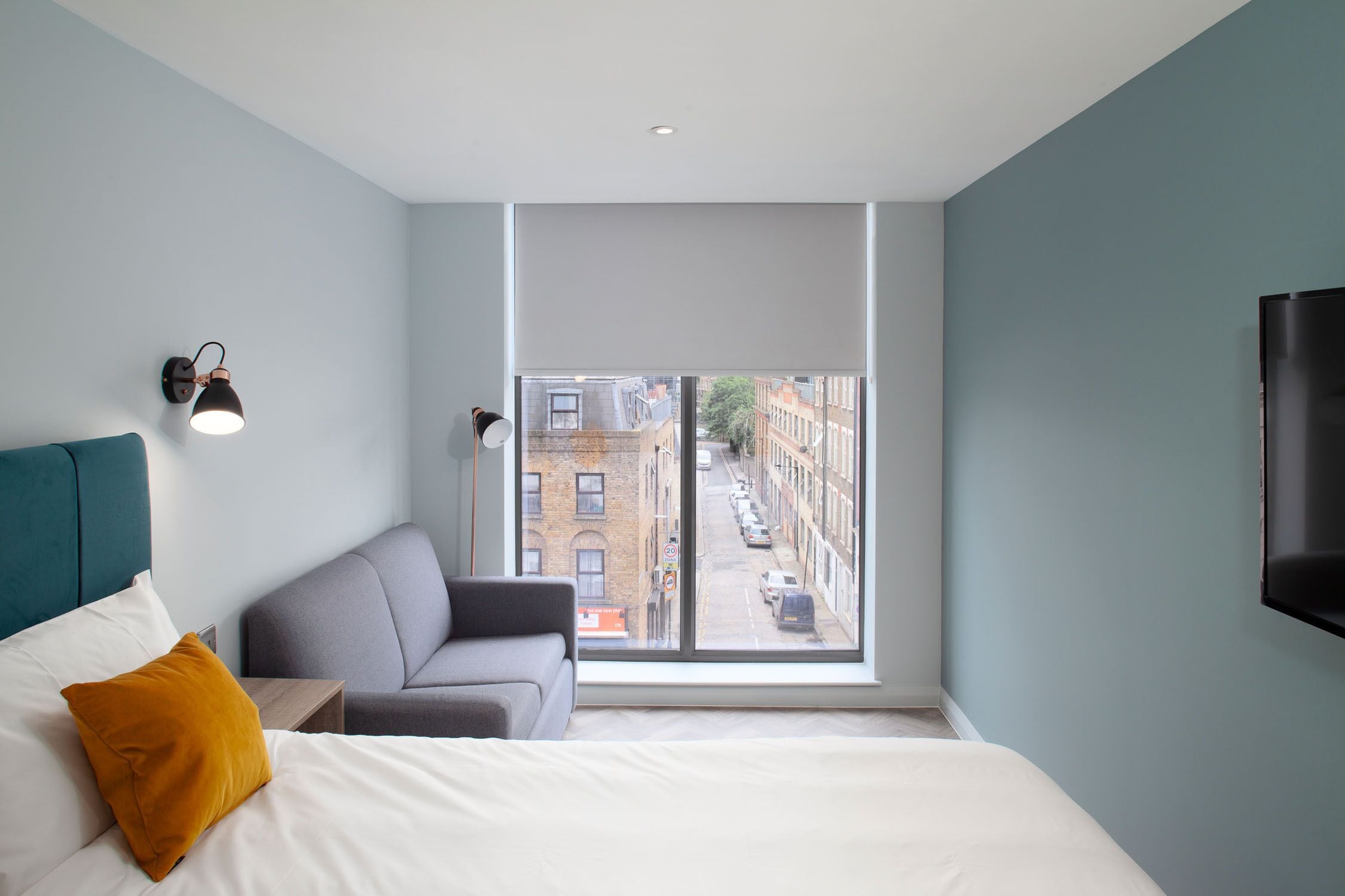 A modern hotel room with a large window, a bed, a sofa, and a TV.