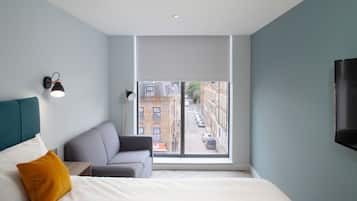 A modern hotel room with a large window, a bed, a sofa, and a TV.