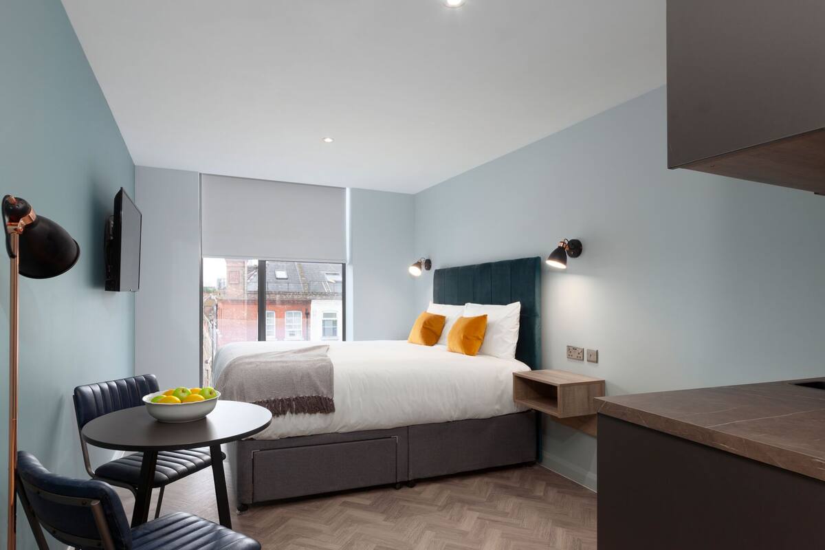 A modern bedroom with a bed, bedside table, and a window with a city view.
