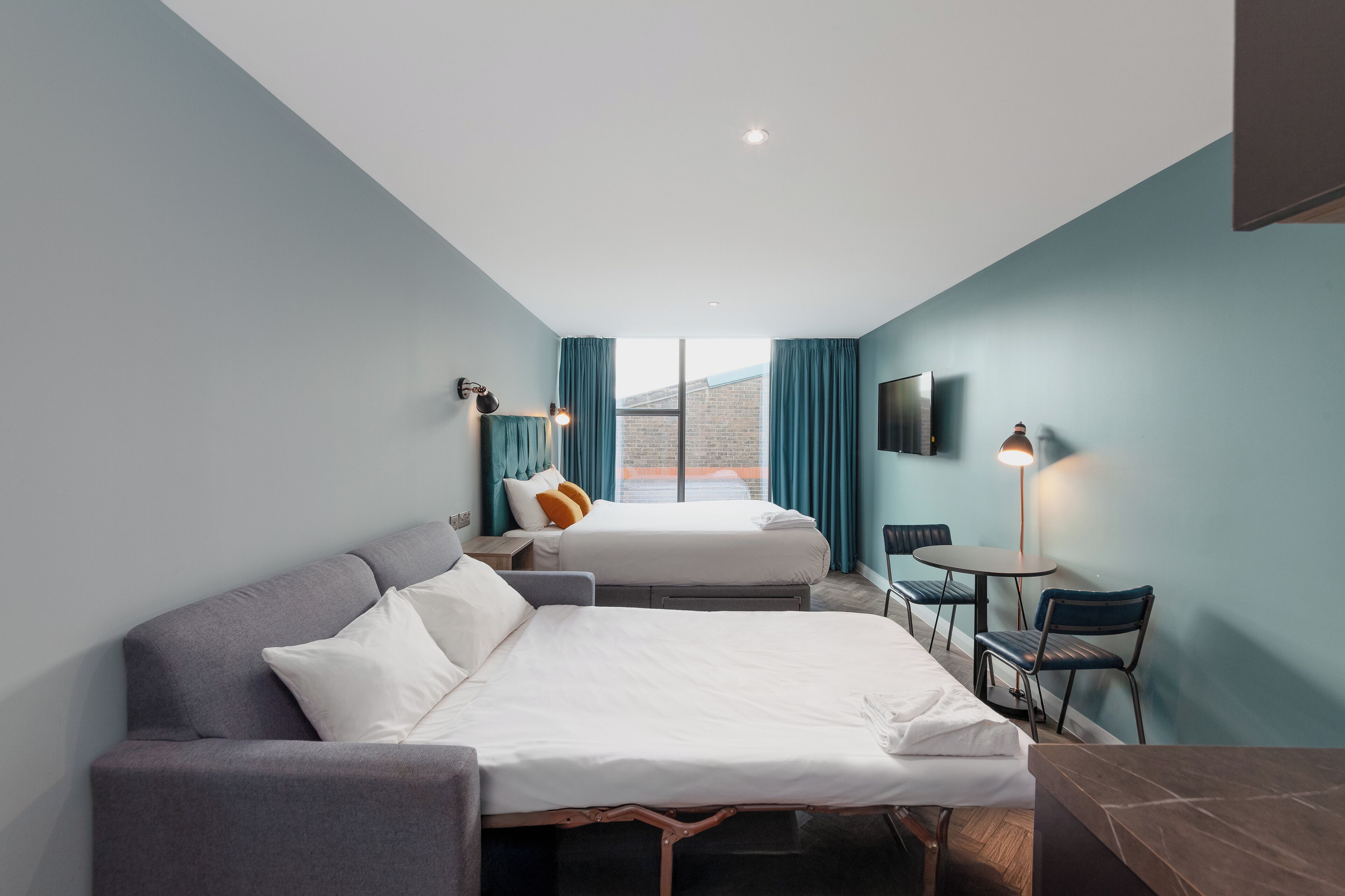 A hotel room with two beds, a desk, a chair, and a TV.