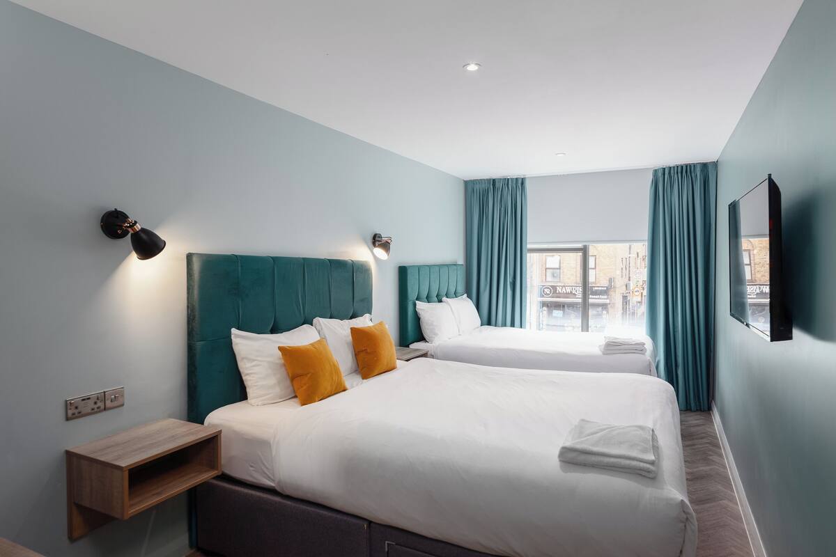 A hotel room with two beds, teal curtains, and a city view.