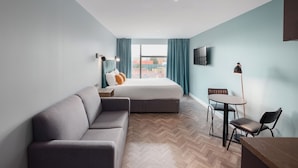 A modern hotel room with a large bed, a sofa, a small table with chairs, and a TV on the wall. - Aptel East (London)