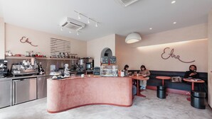 A modern cafe interior with a pink counter, seating area, and a wall with the name 'Eira' displayed. - Aptel East (London)