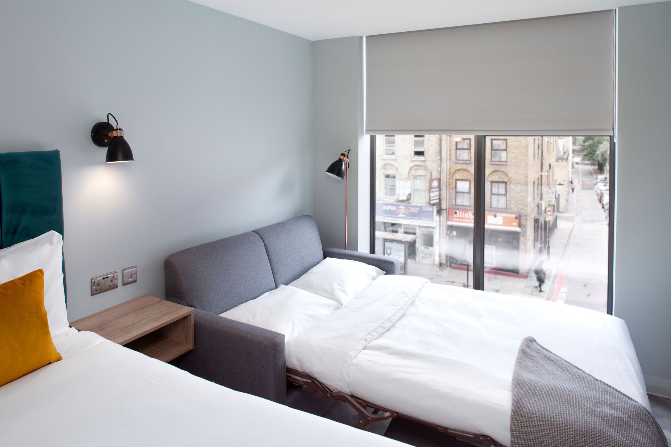 A modern hotel room with a large bed, a small desk, a chair, and a window with a city view.