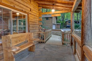 Une cabane en bois dotée d’un porche en pierre, de bancs en bois et offrant une vue sur la forêt environnante.