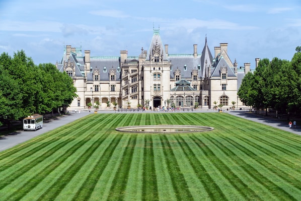 A large, historic building with a symmetrical facade, a central courtyard with a circular fountain, and a well-maintained lawn.