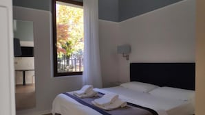 A hotel room with a bed, a window with curtains, a bedside table, and a wall-mounted light. - San Leonardo Suites (Verona)