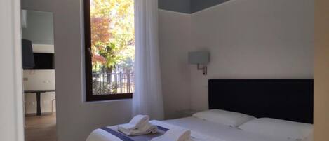 Ein Hotelzimmer mit Bett, Fenster mit Vorhängen, Nachttisch und Wandleuchte.