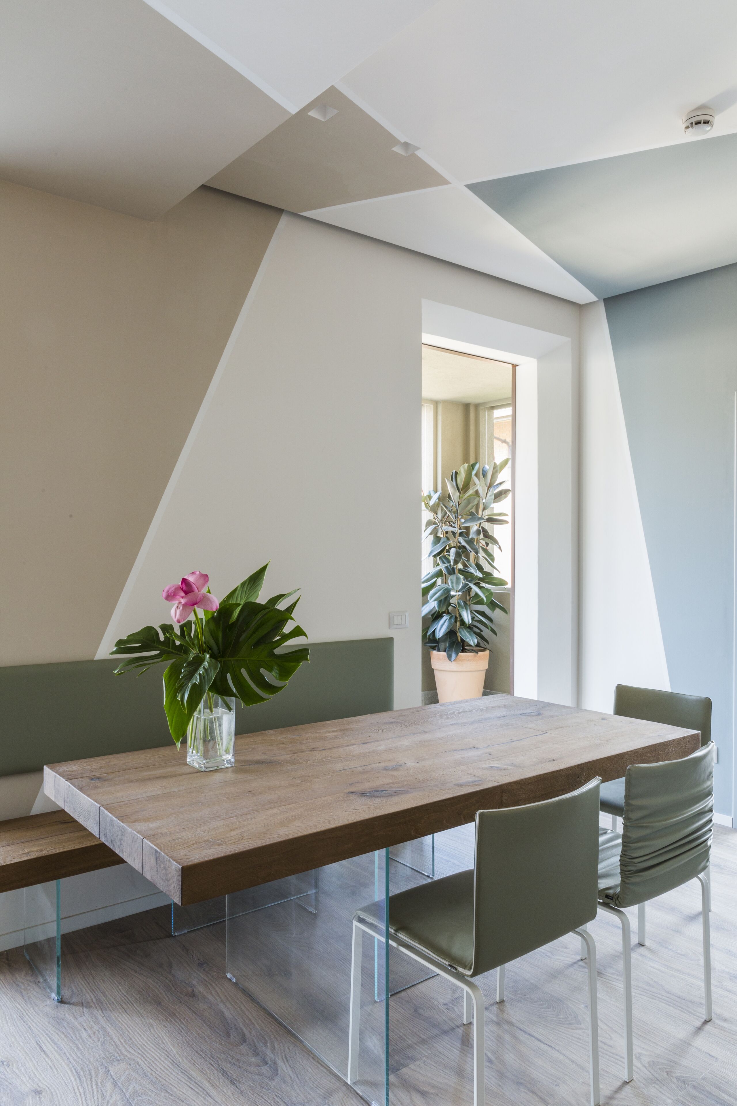 A modern dining area with a wooden table, clear glass chairs, a potted plant, and a bench.