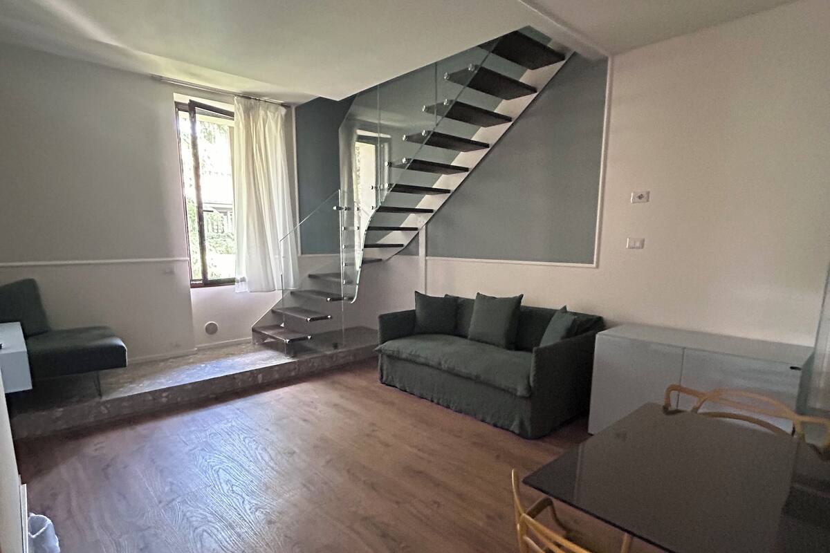 Un espace de vie moderne avec un plancher en bois, un escalier, un canapé et une table à manger avec des chaises.