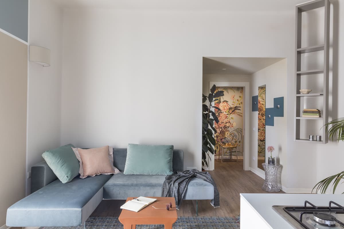 Un salon moderne avec un canapé gris, une petite table en bois et un coin cuisine équipé d’une cuisinière à gaz.