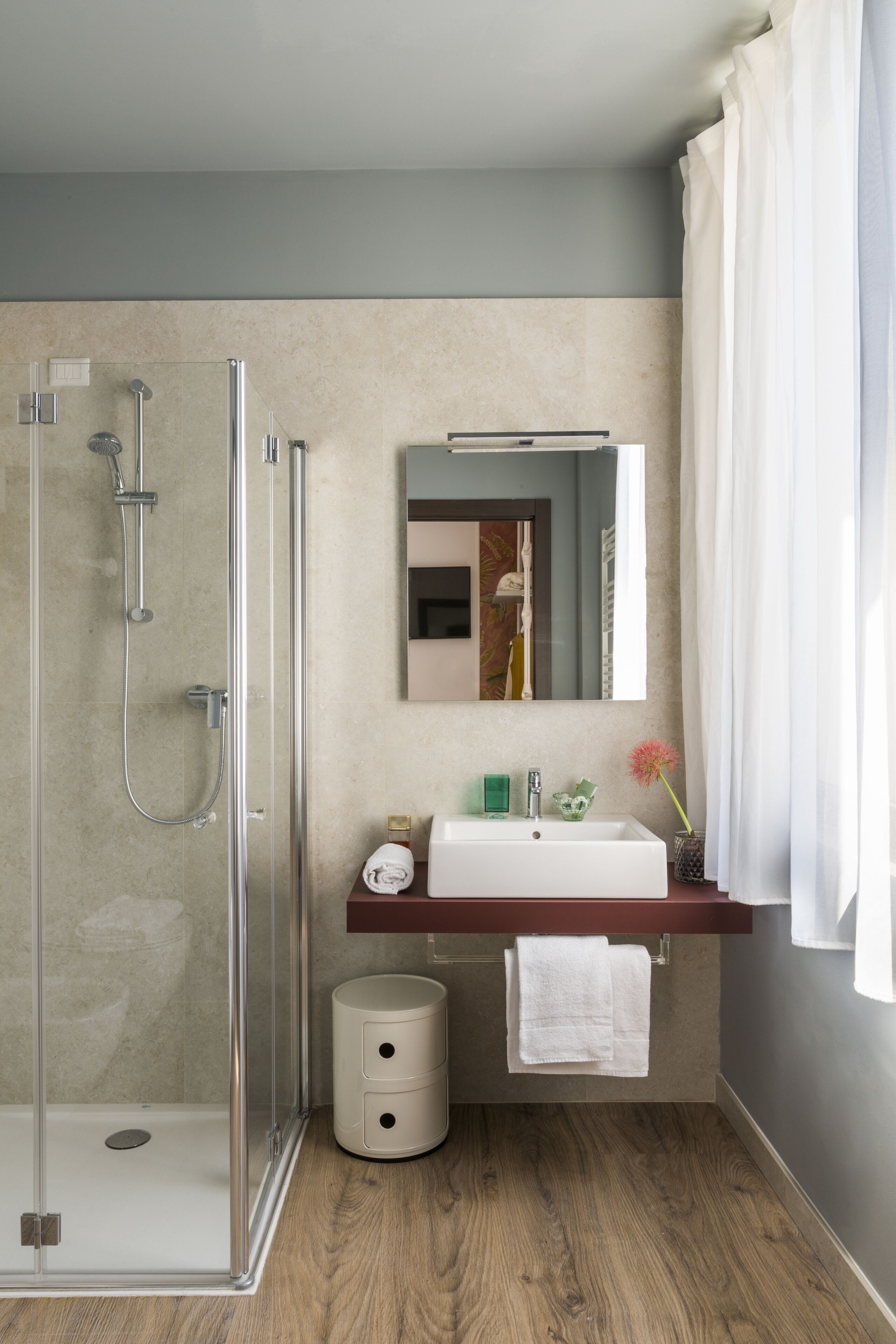 Un baño moderno con ducha de vidrio, un lavamanos blanco y un espejo encima.