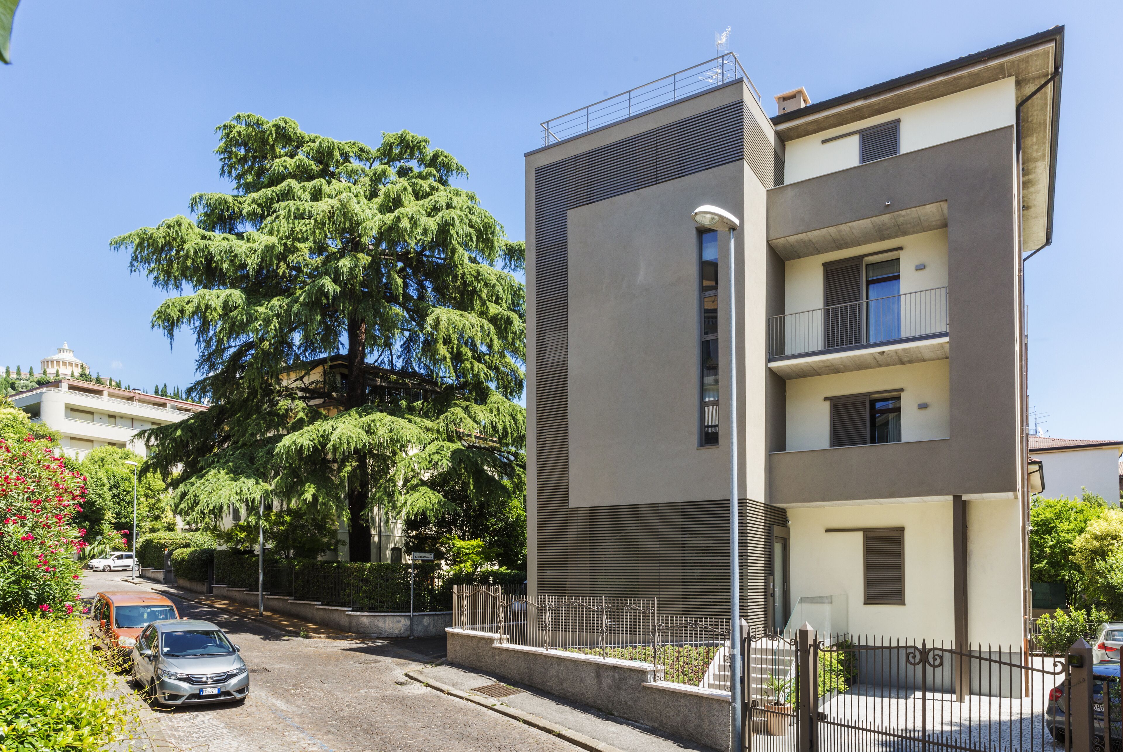 Ein modernes, zweistöckiges Gebäude mit einem Balkon im oberen Geschoss, einem verschlossenen Eingang und einer Straße mit geparkten Autos.
