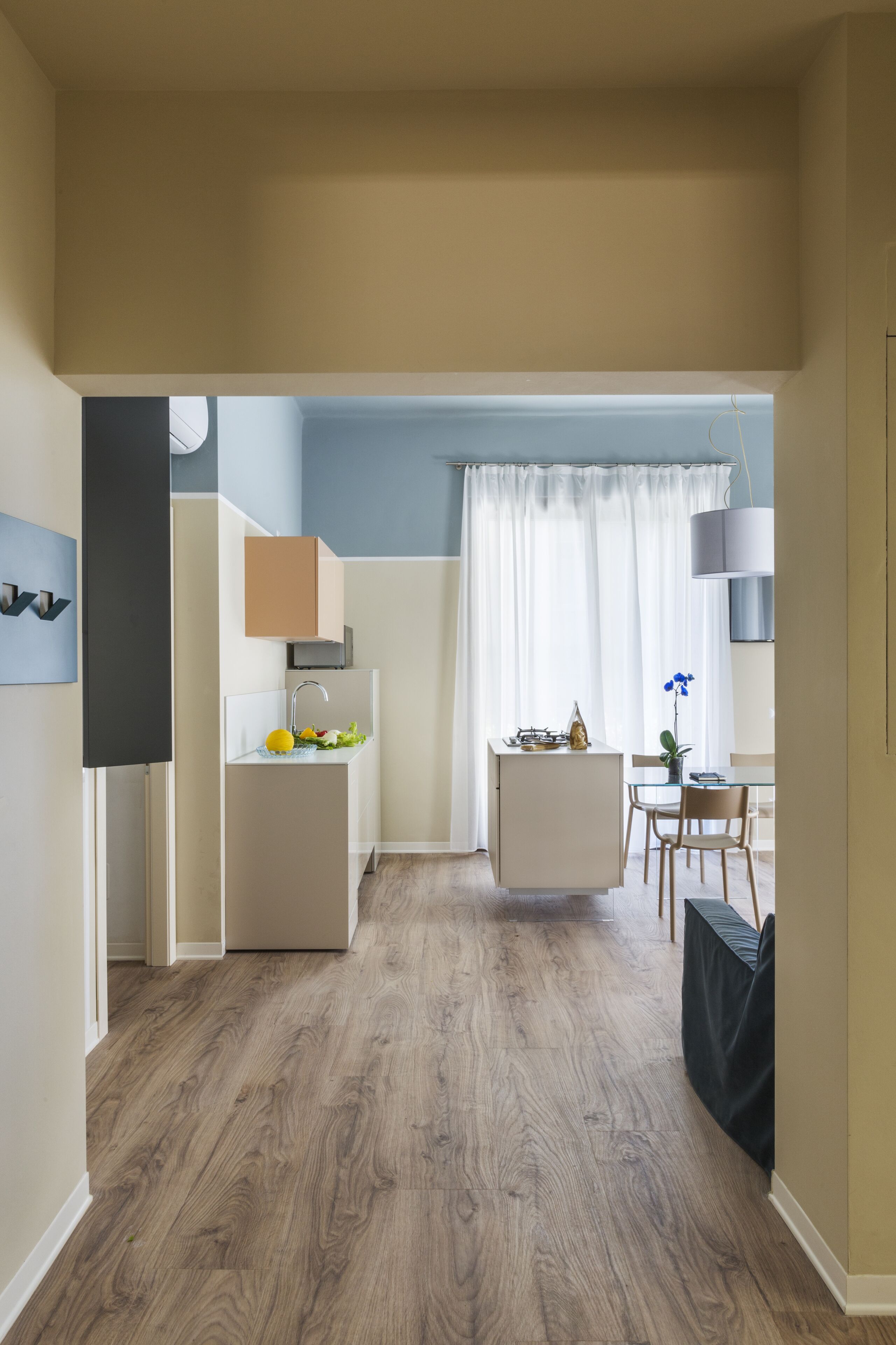 A modern kitchen with a central island, a dining area with a table and chairs, and a view through a doorway to a living space.