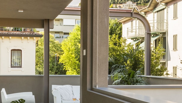 A modern outdoor seating area with a table and chairs, a potted plant, and a view of a hilltop building. - San Leonardo Suites (Verona)