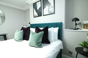 A modern hotel room with a teal upholstered headboard, a round mirror, and abstract artwork on the wall.