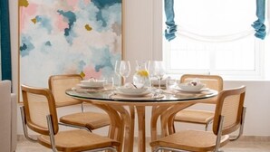 A dining area with a round glass table, six wicker chairs, and a large abstract painting on the wall.