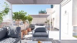 An outdoor patio with a sofa and chairs, potted plants, and a table with fruit.