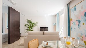 A modern living room with a sofa, dining table set with glasses and plates, a plant, and a TV.