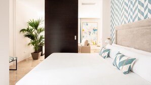 A modern hotel room with a large bed, a potted plant, a sofa, and a painting on the wall.