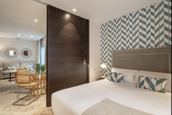 Un dormitorio moderno con una cama grande, una zona de comedor con una mesa de vidrio y una pared con diseño.