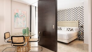 A modern hotel room with a glass dining table, wicker chairs, a bed with patterned bedding, and a large artwork on the wall. - Hommyhome Vera Cruz 101 (Sevilla)