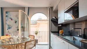 Cocina moderna con una mesa de comedor de vidrio, sillas de mimbre y vistas a un edificio tradicional a través de una puerta abierta.