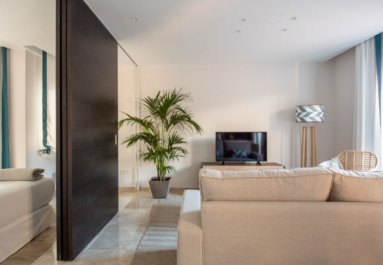 En moderne stue med sofa, fjernsyn, en potteplante og en gulvlampe.