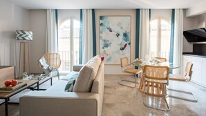Una sala de estar moderna con sofá, mesa de comedor y sillas, ventanas amplias con cortinas, y un cuadro en la pared.